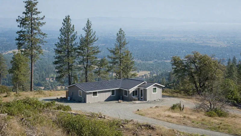 Butte County, California: Pine ridge above a hazy flat valley; newer house with metal roof and gravel yard; young shrubs on slopes