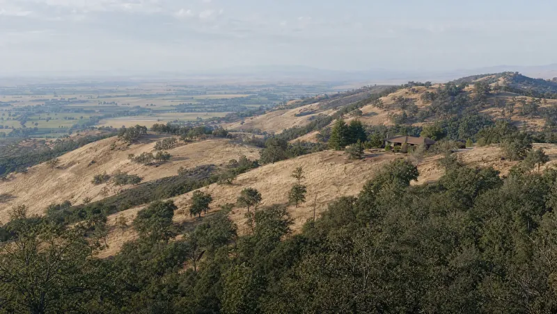 Colusa County, California: Dry blue-oak and chaparral foothills over golden grass; ranch house; flat valley below