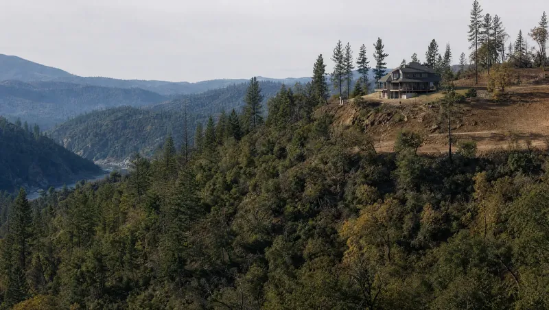 El Dorado County, California: Sierra foothills: ponderosa pines, oaks, manzanita; a two-story house on a wooded ridge with cleared ground around it; canyon below