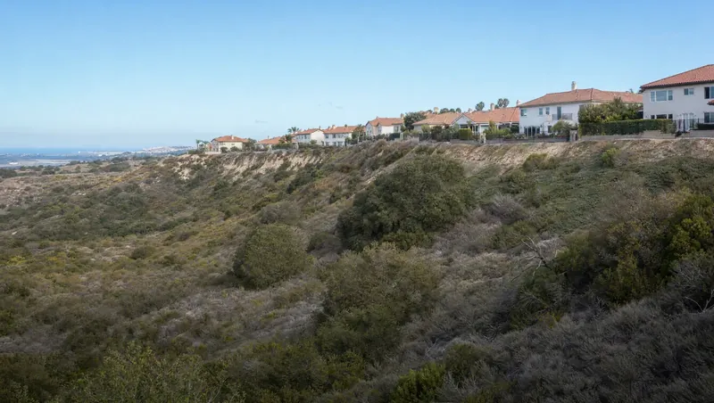 Orange County, California: Sage-scrub canyon with live oaks; suburban tile-roof homes lining the ridge right next to wildland