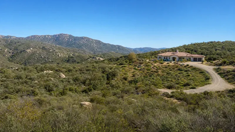 San Diego County, California: Granite-boulder hills covered in chaparral and sage scrub; single-story ranch house with tile roof and gravel drive