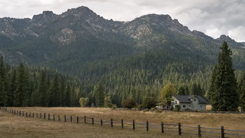 Siskiyou County, California: Dense fir/pine mountain valley, rugged mountains; rural home at a meadow edge with a wooden fence