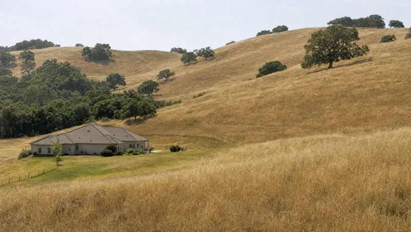 Solano County, California: Grassy rolling hills with scattered oaks; home at the grassland edge with a mowed strip