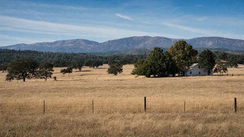 Tehama County, California: Wide golden oak savanna with ranch fencing; farmhouse with shade trees; forested mountains far away