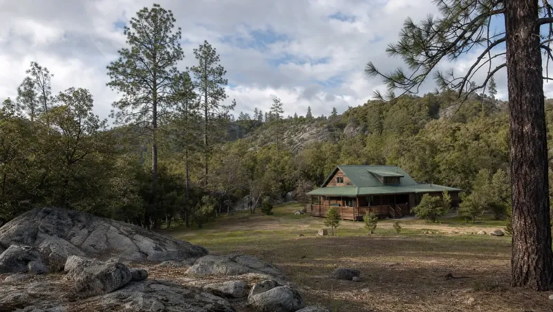 Tuolumne County, California: Mixed conifer forest with granite outcrops; cabin-style home with green metal roof and cleared yard